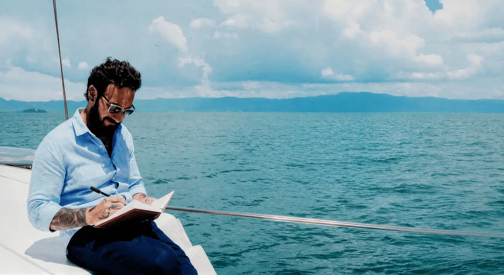 Gil Pinna escrevendo em um caderno a bordo de um barco em Ilhabela